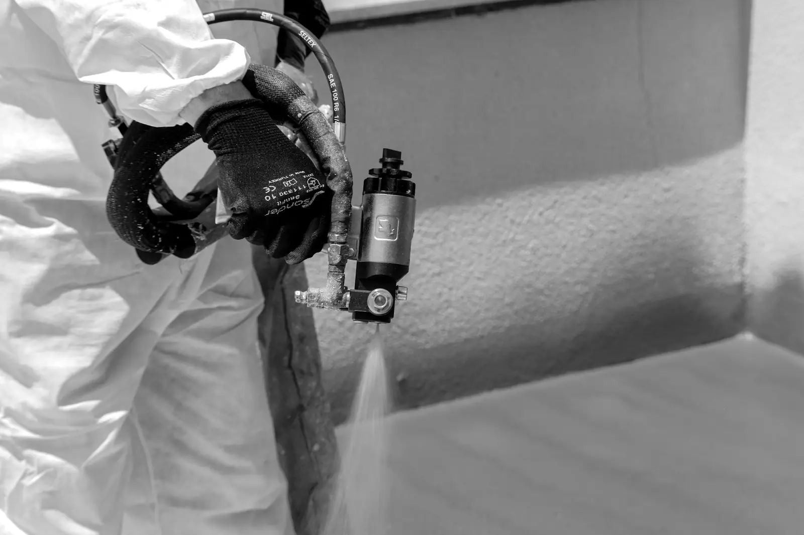 Malíř v ochranném obleku stříká stěnu airless pistolí